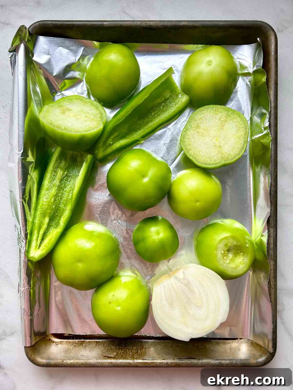 tomatillos, jalapeños, and half an onion on baking sheet.