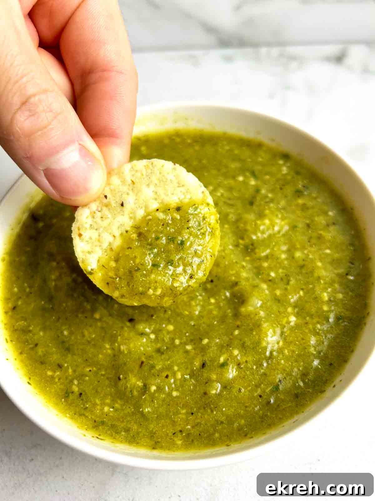chip being dipped into salsa verde in white bowl.