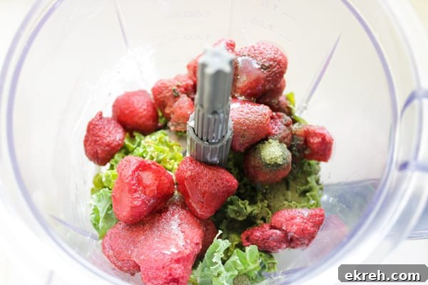 Overhead view of kale and frozen strawberries in blender
