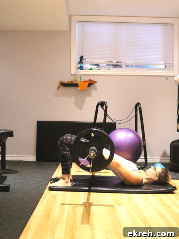 Woman in home gym performing a barbell glute bridge on a black mat
