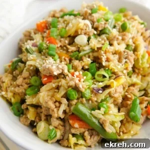 Unstuffed egg roll or pork fried rice presented in a white bowl on white marble countertop. Displayed with chop sticks, sriracha and green onions.