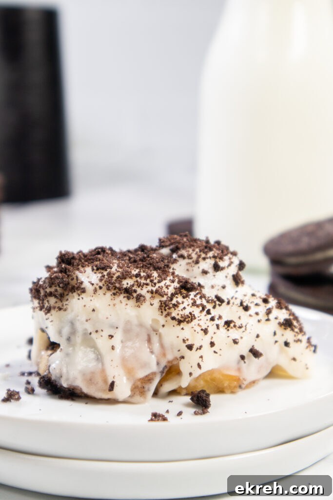 Air Fryer Oreo Cinnamon Rolls with Crunchy Oreo Swirl 2 An Air Fryer Oreo Cinnamon roll on a small white plate topped with cream cheese frosting and crushed Oreo pieces.