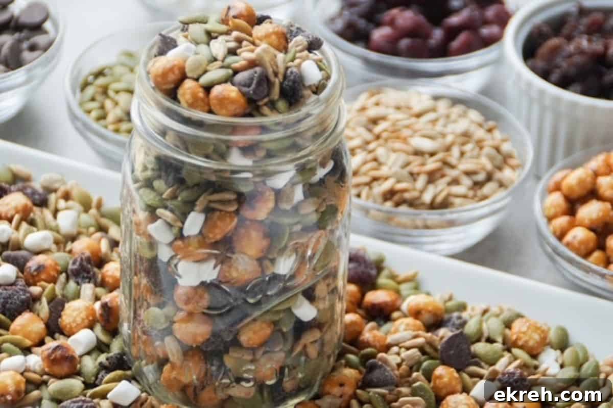 Nut-Free Trail Mix Recipe Kids Will Love 4 One glass mason jar filled with nut-free trail mix surrounded by trail mix on a white plate at its base. Ingredients in separate small glass bowls lined up to the side of the white plate.