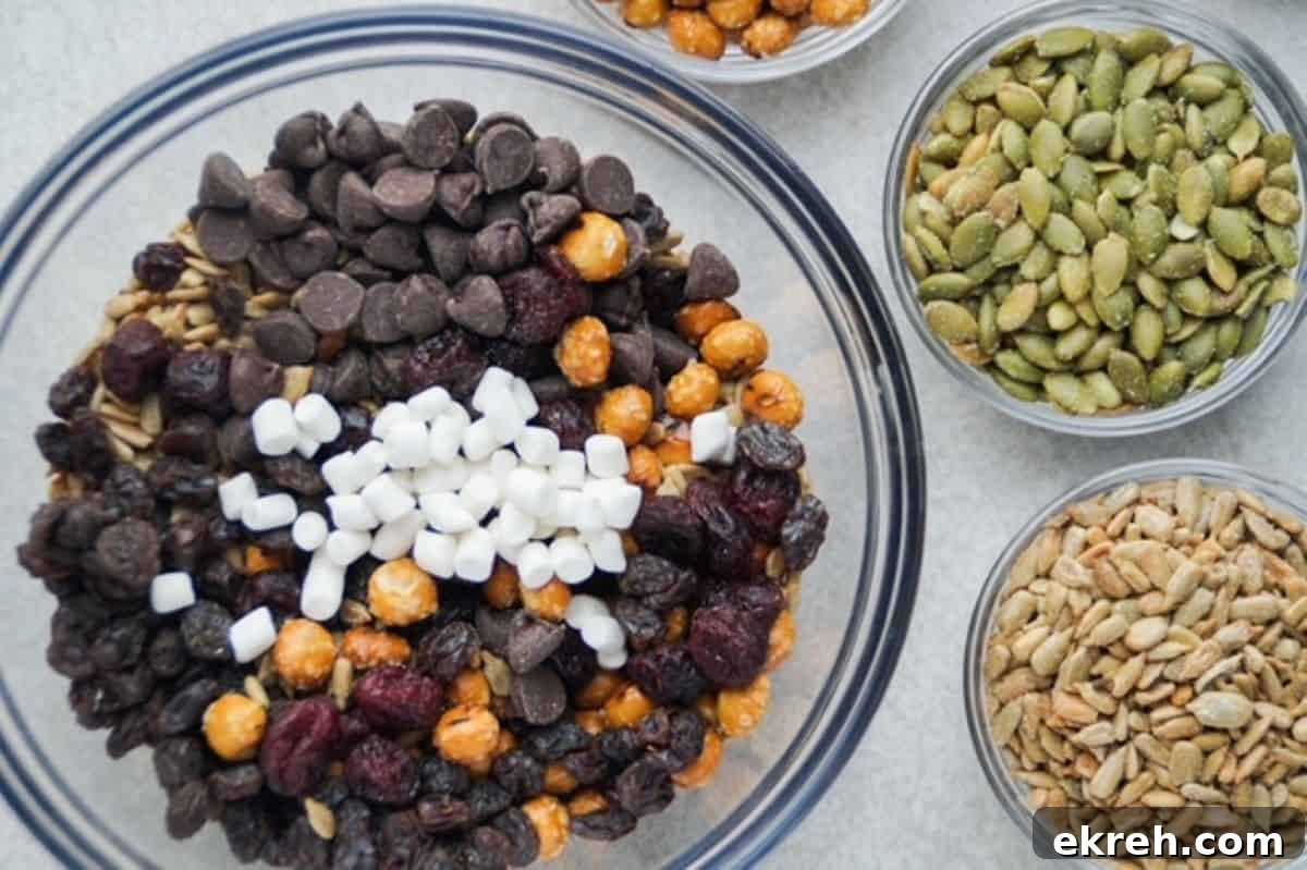 Nut-Free Trail Mix Recipe Kids Will Love 5 Nut free trail mix ingredients in a glass mixing bowl with small glass bowls of pumpkin and sunflower seeds to the right of it.