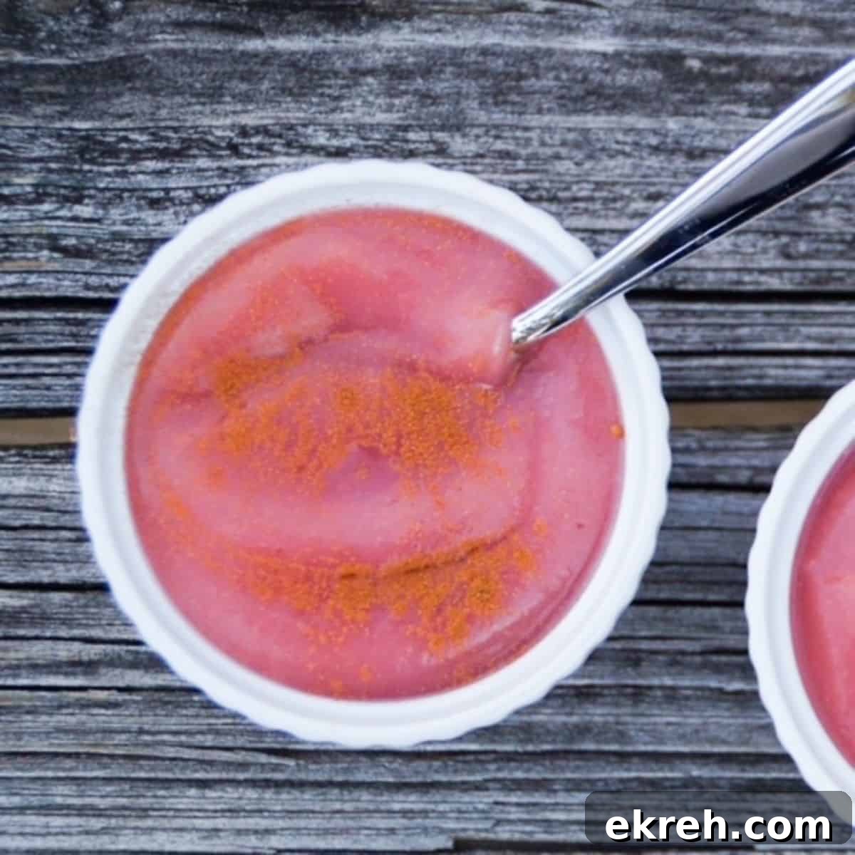 Pink applesauce in a white bowl with a spoon.