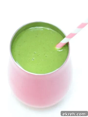 Spinach mango smoothie in a pink tumbler with a pink and white striped straw.