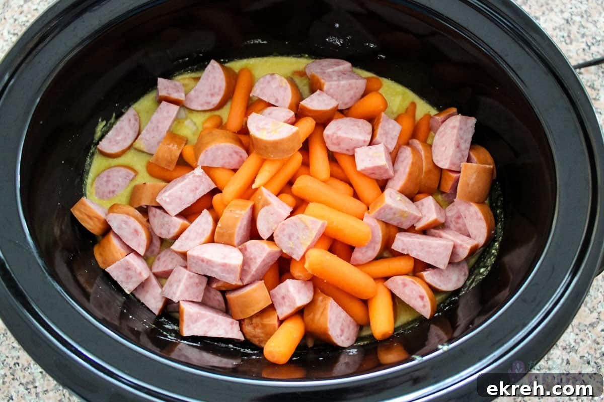 Sausage, onions, and carrots added to slow cooker insert.