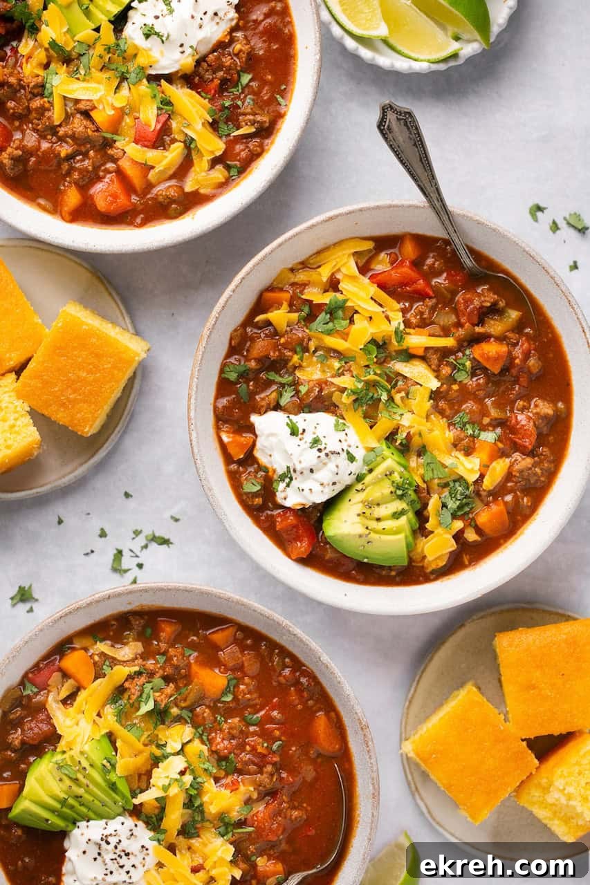 no bean chili in 3 bowls topped with cheese, sour cream, and avocado with cornbread on the side