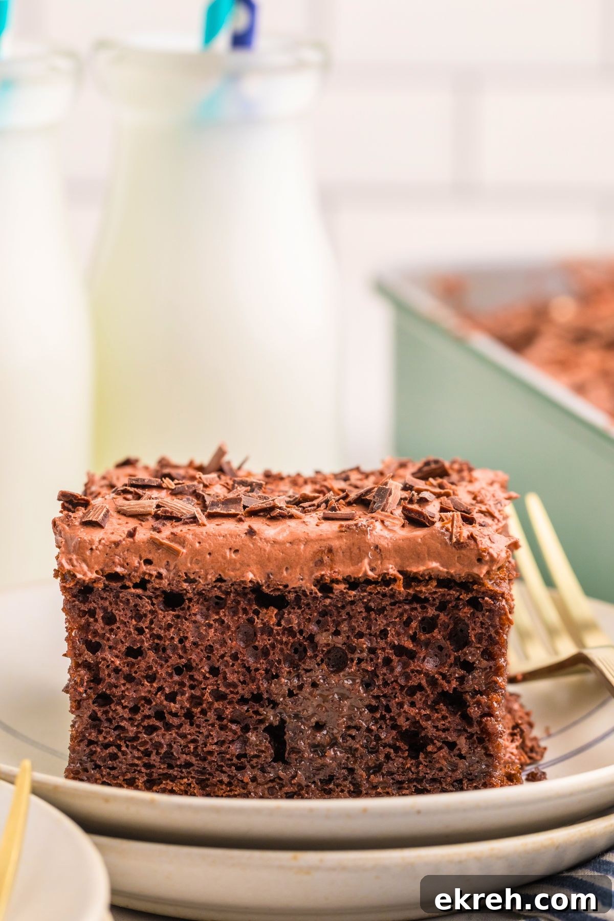 Chocolate poke cake on a plate with bottles of milk behind the plate. 