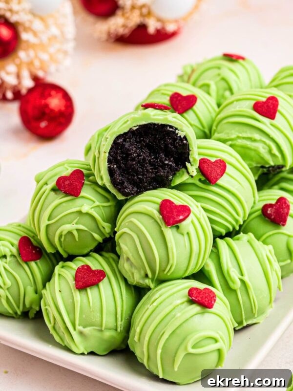 Green coated Grinch Oreo balls with a red candy heart, stacked on a plate.