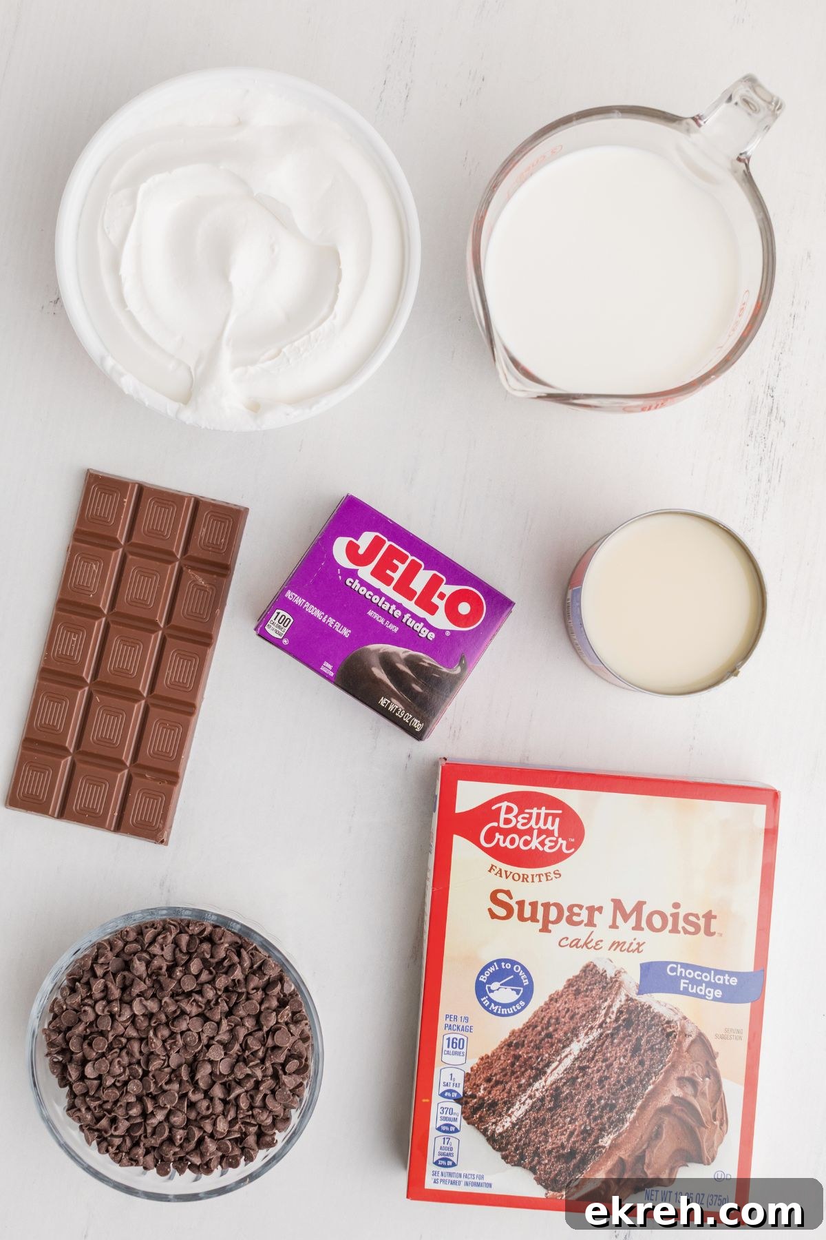 Ingredients needed to make chocolate poke cake, on a white marble table. 