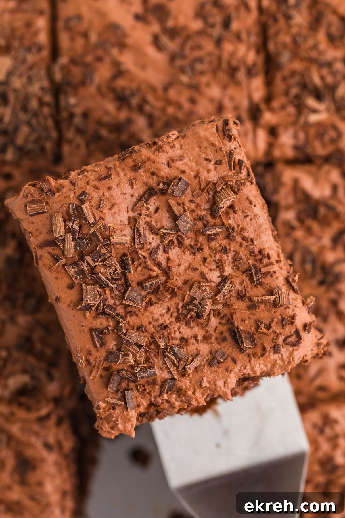 Piece of chocolate poke cake on a spatula topped with whipped cream and chocolate shavings. 