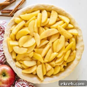 How to Make Apple Pie Filling from Scratch 13 An overhead image of apple pie filling in a raw pie crust with apples and cinnamon sticks around it.