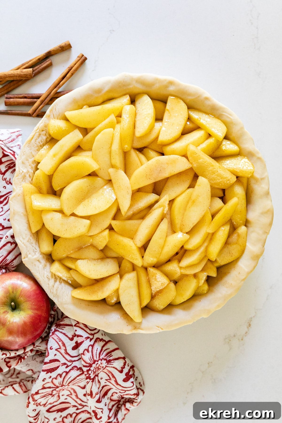 How to Make Apple Pie Filling from Scratch 3 An overhead image of apple pie filling in a raw pie crust with apples and cinnamon sticks around it.
