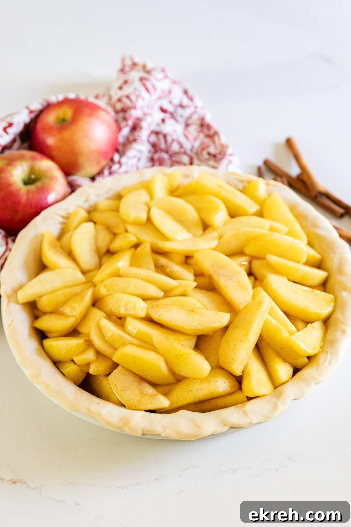 How to Make Apple Pie Filling from Scratch 8 Apple pie filling in a raw pie crust with apples and cinnamon sticks behind it.
