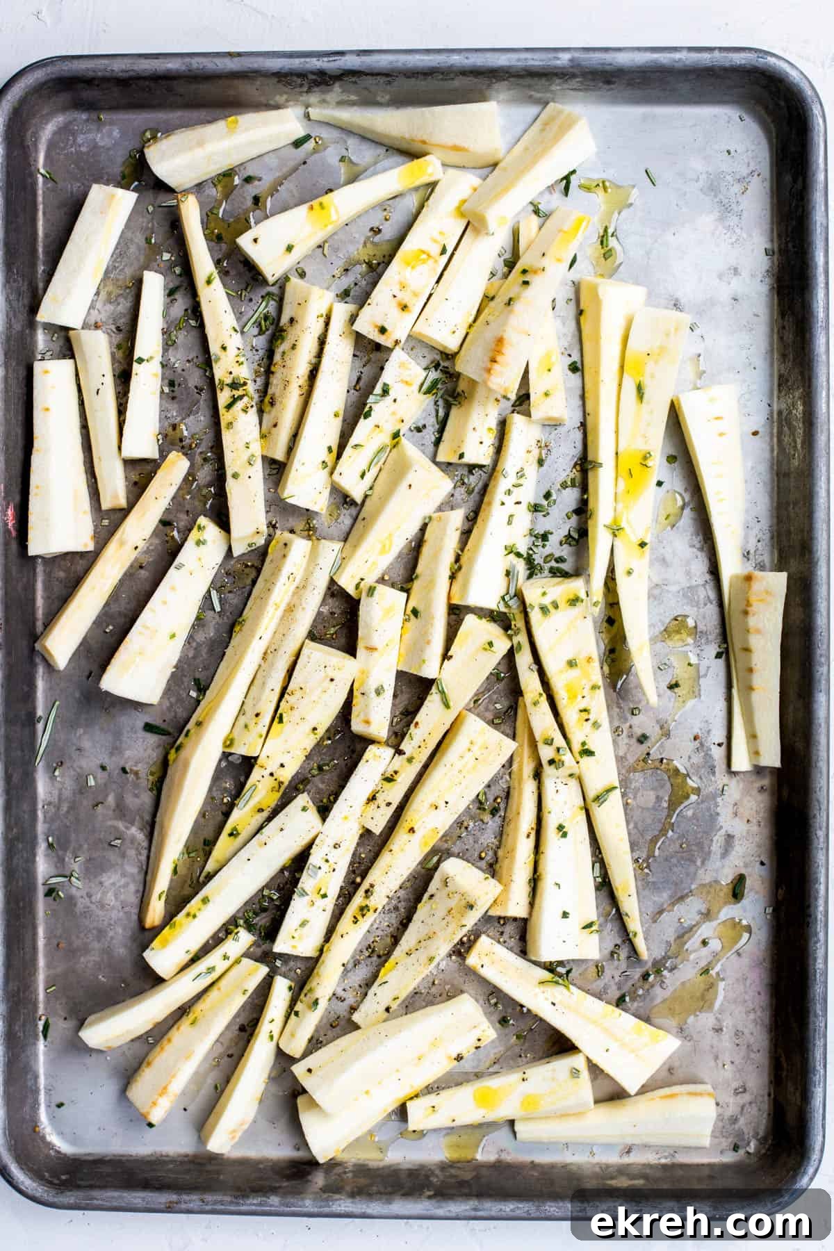 Crispy Oven-Roasted Parsnips with Garlic and Herbs 4 sliced parsnips on a baking sheet with olive oil and fresh herbs