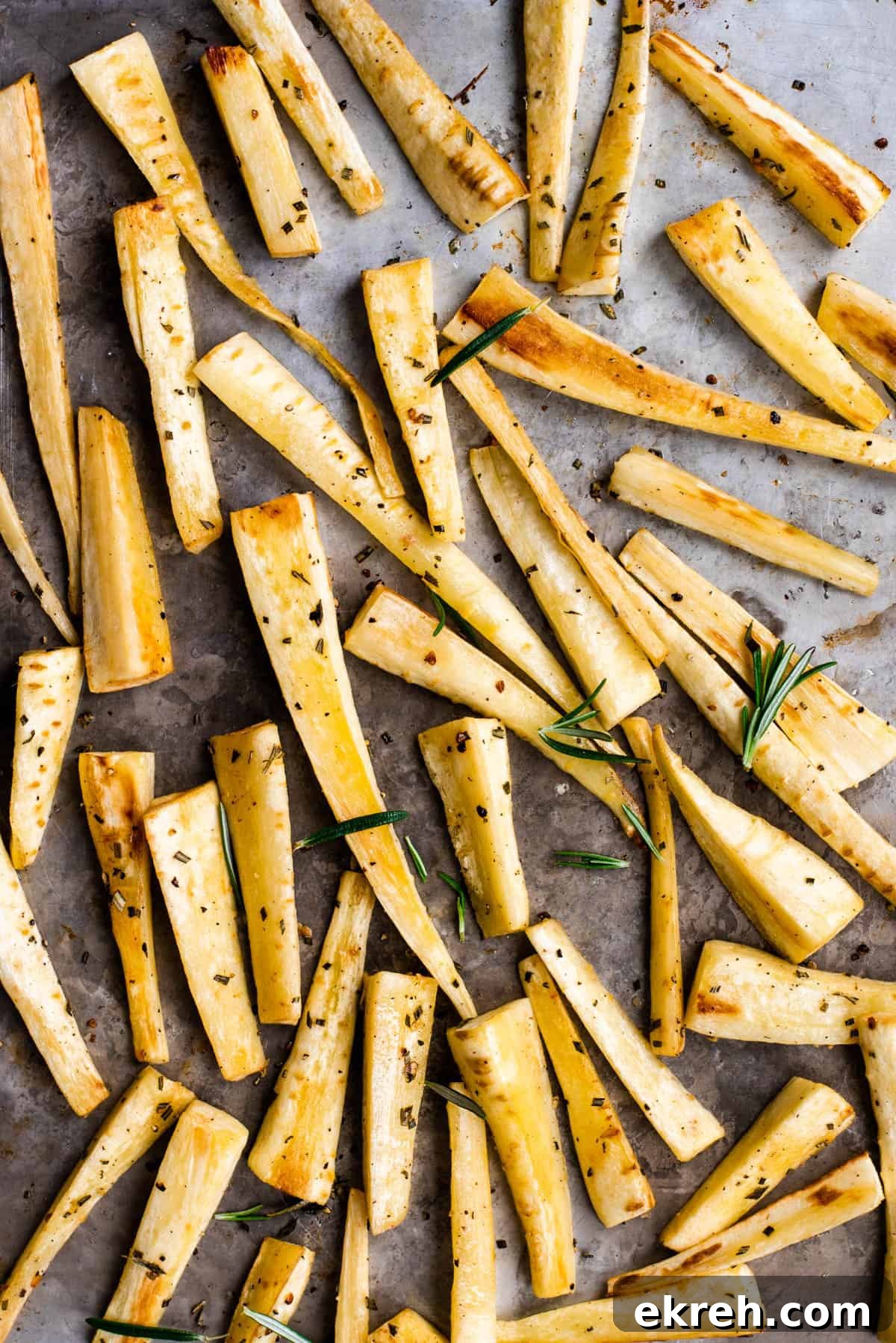 Crispy Oven-Roasted Parsnips with Garlic and Herbs 5 roasted parsnips on a baking sheet with rosemary