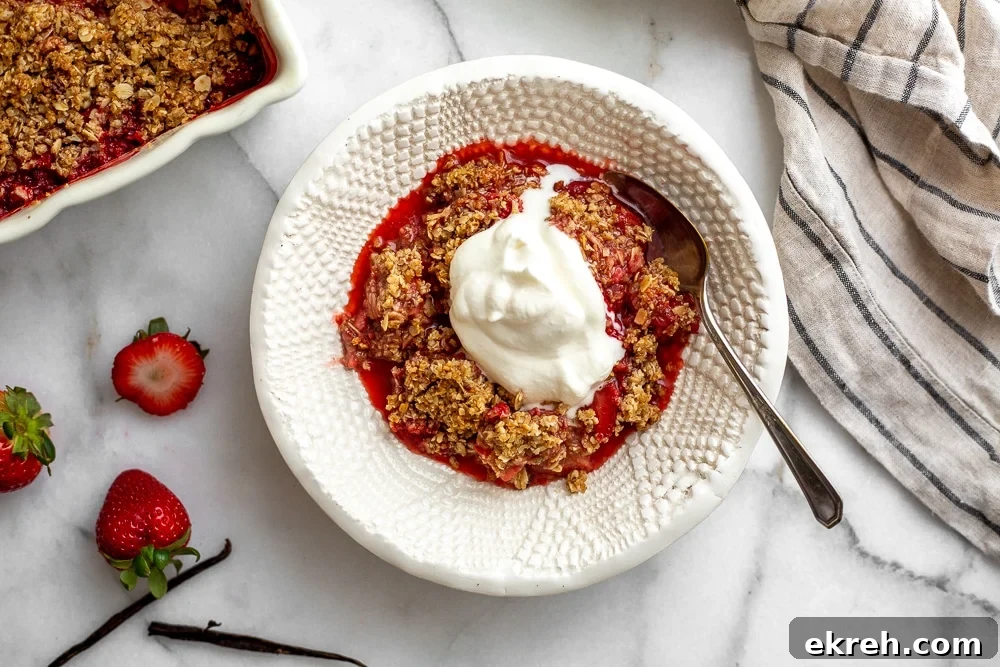 A serving of gluten free strawberry crisp in a serving bowl with a dollop of whipped cream
