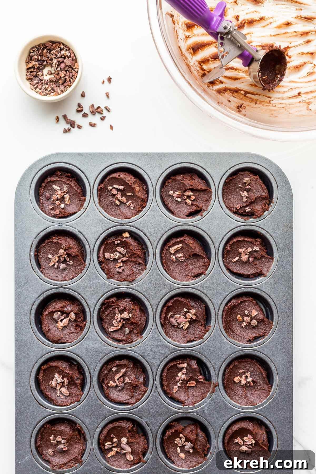 Garnishing chocolate financiers with cocoa nibs before baking them.