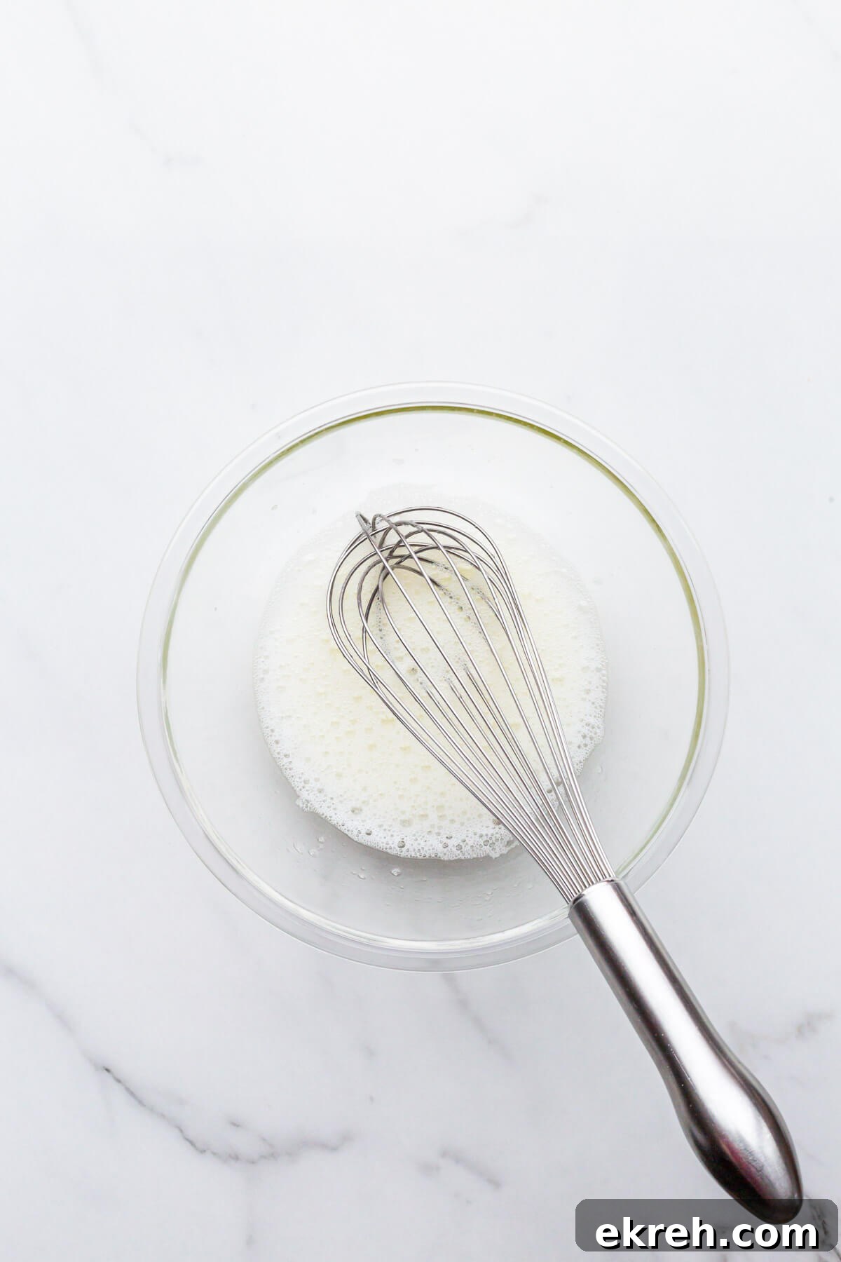 Whipping egg whites in a glass bowl until very frothy and foamy.