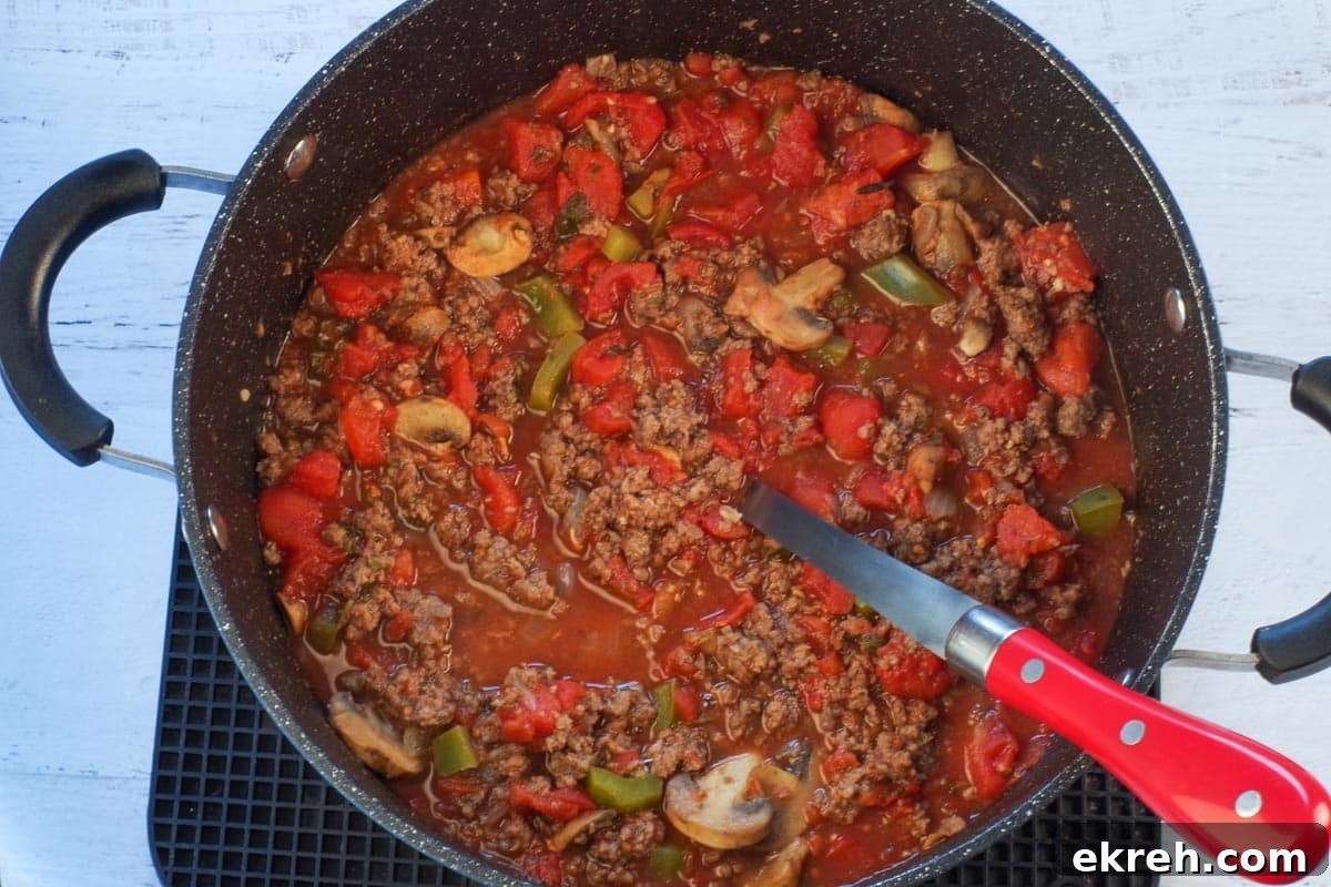 spaghetti sauce with ground beef added in large pot with a spoon