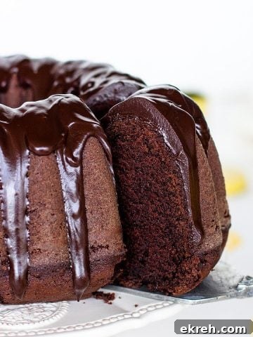 Cake server with slice being pulled out of glazed chocolate bundt cake, white background.
