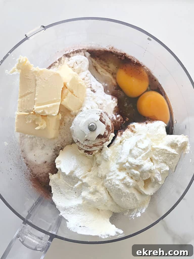 Bowl of food processor with sour cream, butter, eggs, cocoa powder and flour mixture. Top view.