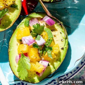 Closeup of Avocado Pineapple Salsa Boats on a teal plate with colorful plate and tablecloth underneath