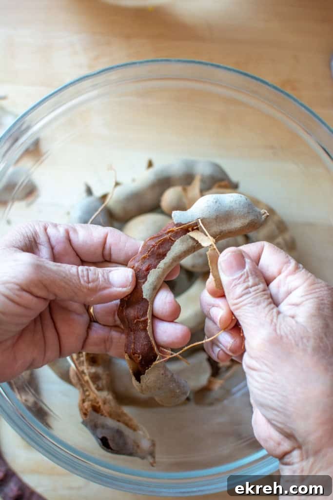 Tamarind Agua Fresca Recipe: Agua de Tamarindo 5 A hand peeling the hard shell off the tamarind pods