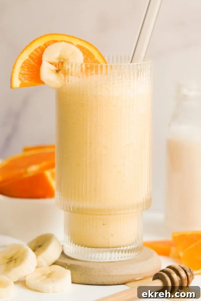 orange banana smoothie in a glass surrounded by banana and orange slices