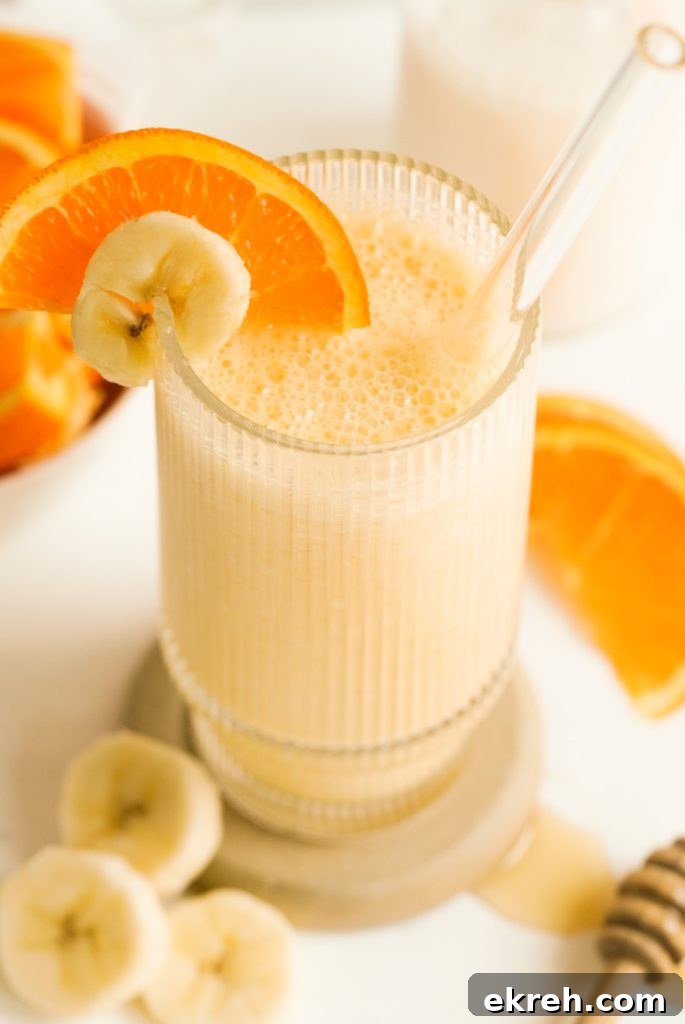 banana and orange banana smoothie in a glass with a glass straw