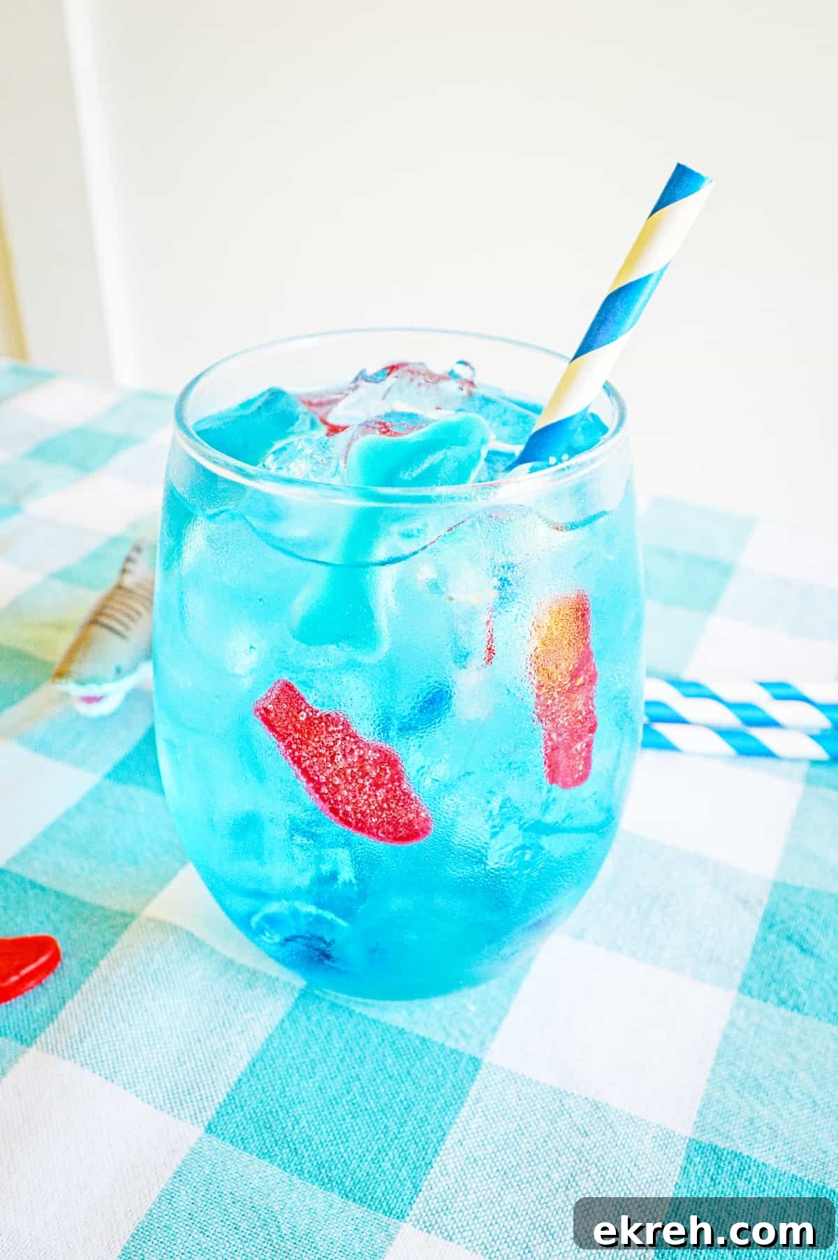 Blue ocean water drink in glass with ice, gummy fish, gummy shark, and blue and white paper straw