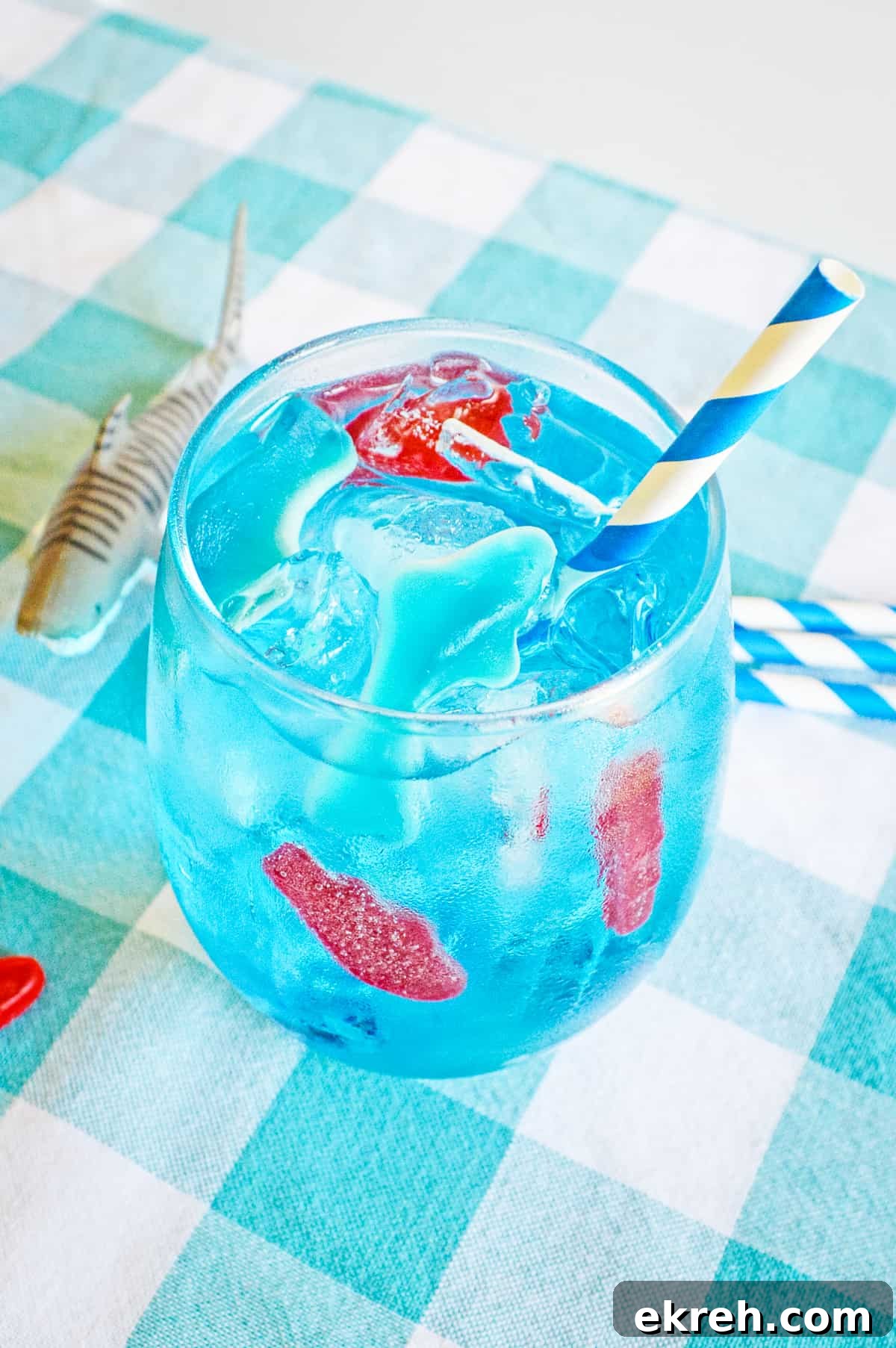 Homemade version of Sonic's ocean water drink in a glass with ice, swedish fish, gummy shark, and blue and white paper straw