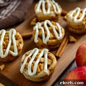Apple Pie Filled Cinnamon Rolls with Caramel Glaze 10 Five baked and frosted apple pie cinnamon rolls on wooden cutting board with some cinnamon sticks and fresh red apples on the side as garnish.