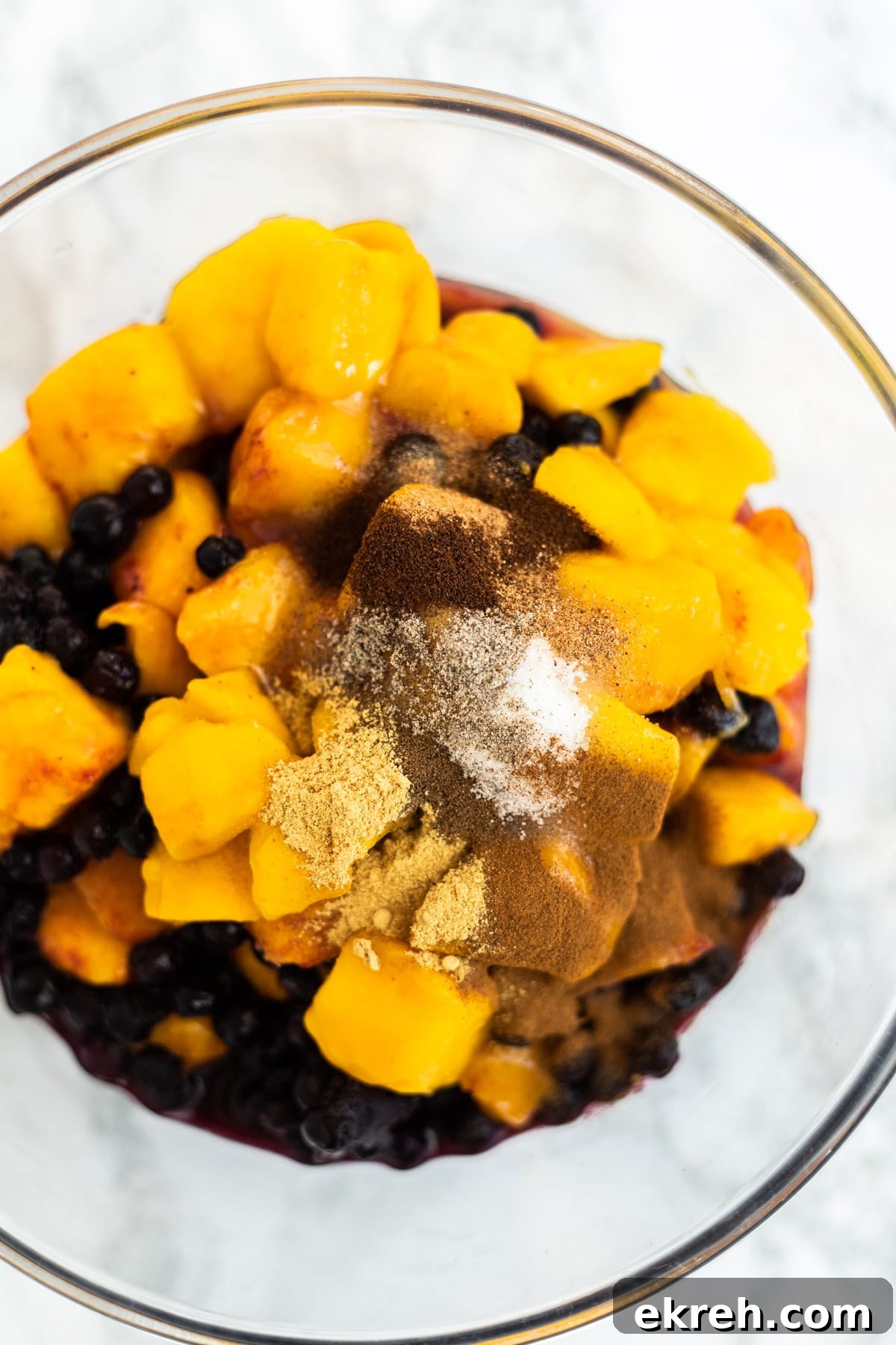 A top down view of a bowl of mangos and blueberries topped with sugar and spices.