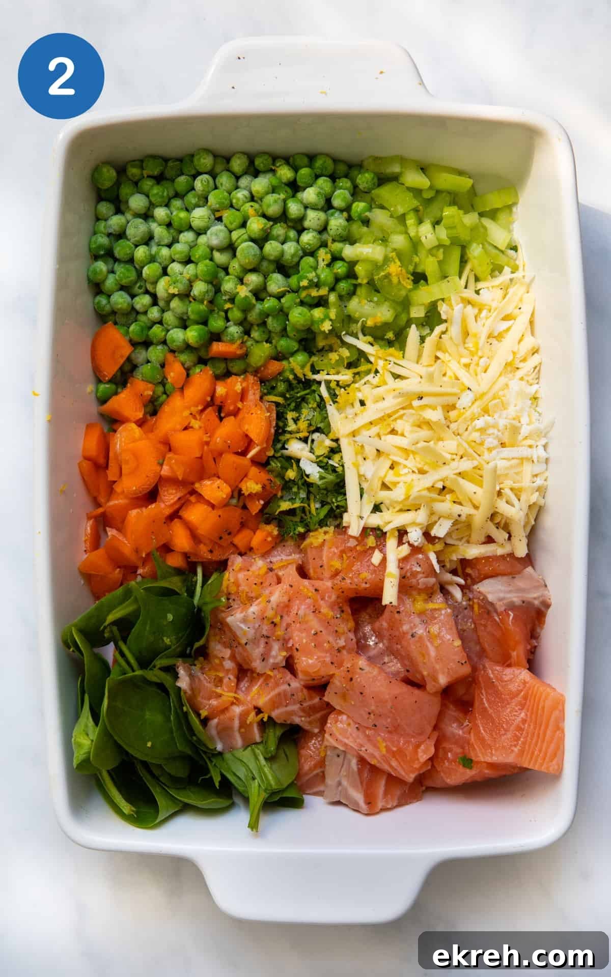 Salmon, spinach, cheese, carrot and peas in a baking dish.