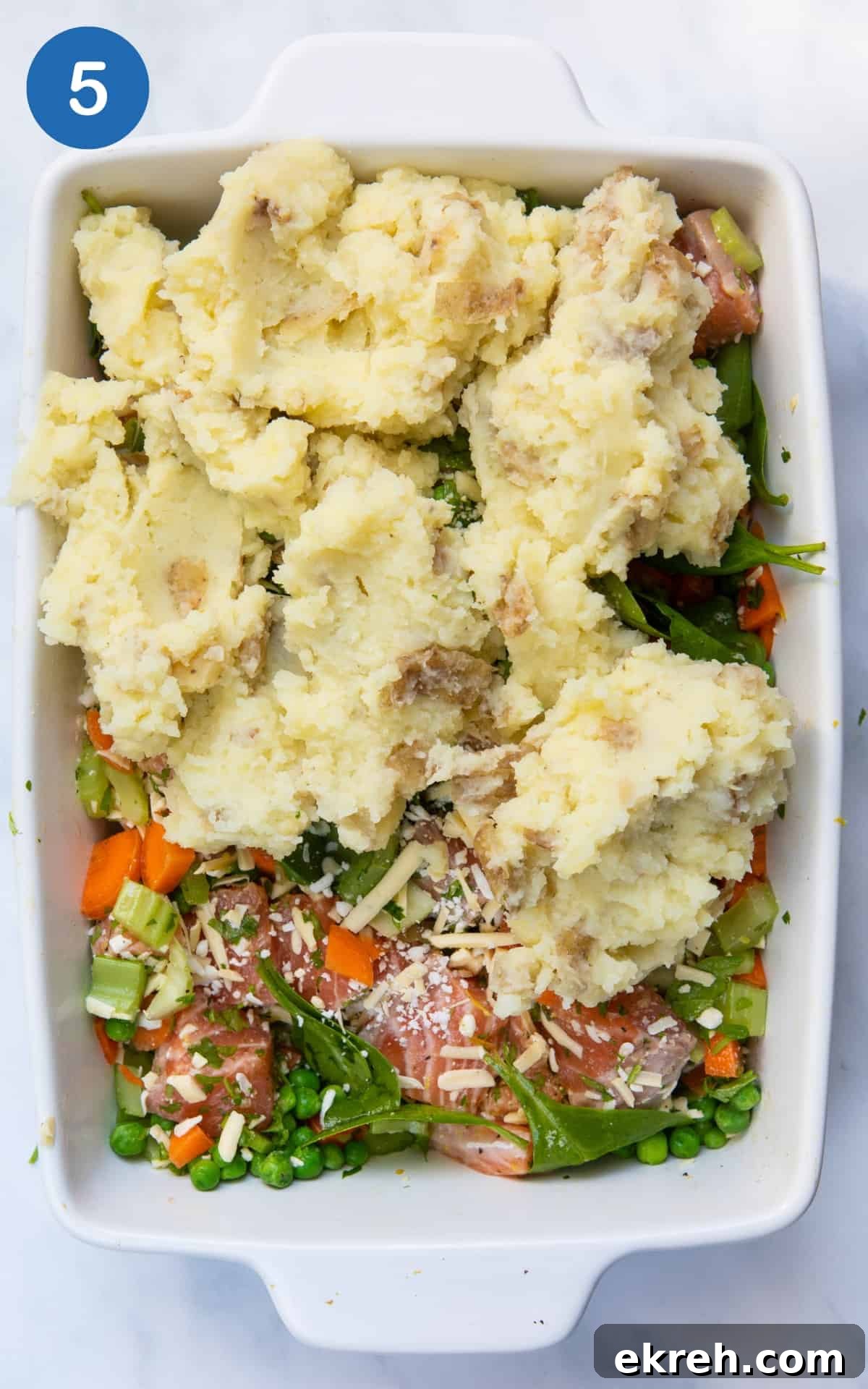 Salmon and vegetables in a dish with mashed potatoes on top.