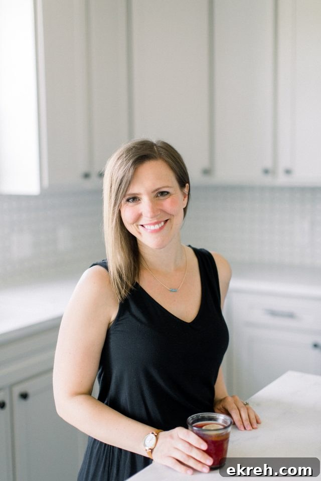 A white kitchen with CEO, Erin Jensen, standing at the kitchen island.