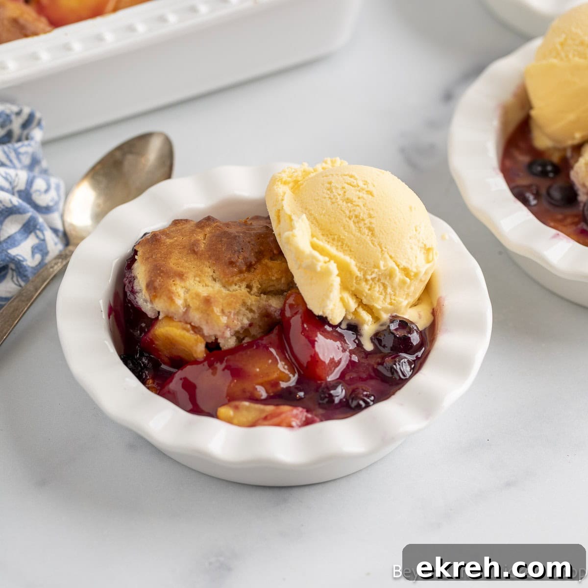 Blueberry Peach Cobbler with a scoop of vanilla ice cream in a white dish.