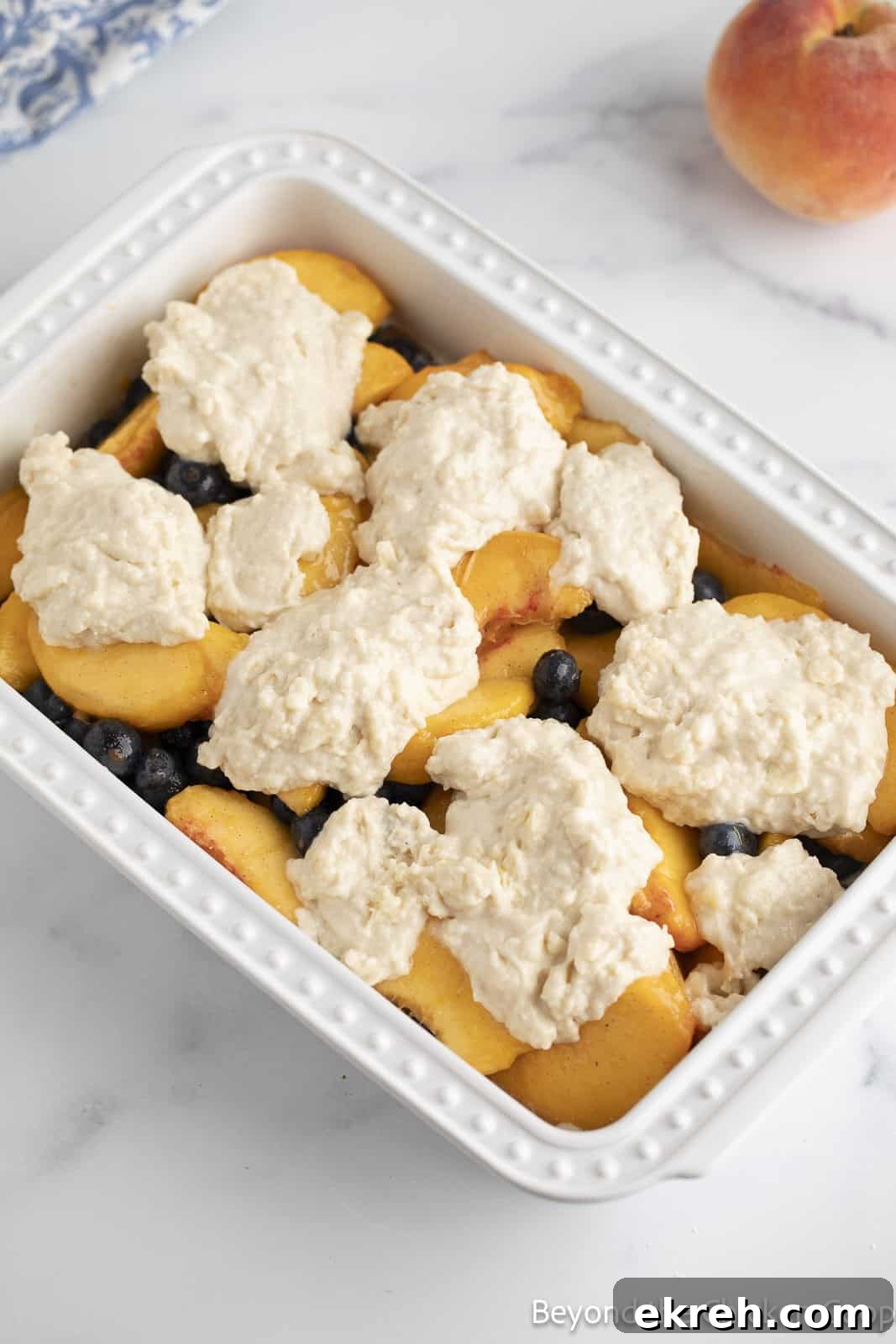 Dollops of cobbler batter on top of a layer of fruit. 