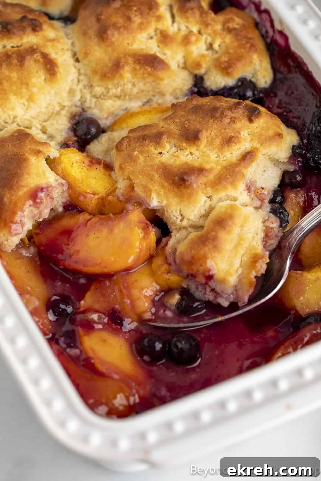 Peach cobbler with blueberries in a white dish.