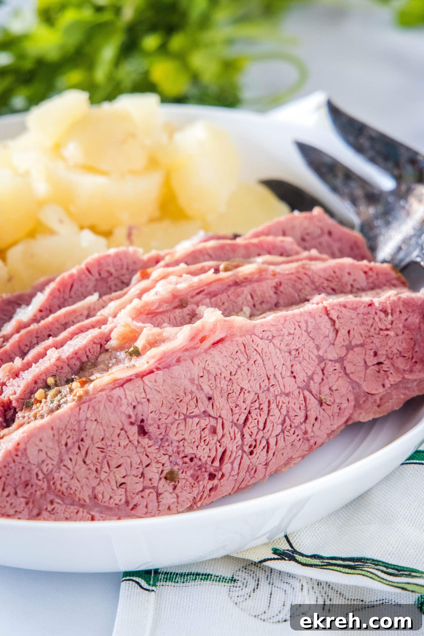Slow Cooker Corned Beef Sliced corned beef on a white plate next to a fork, with cooked onions in the background.