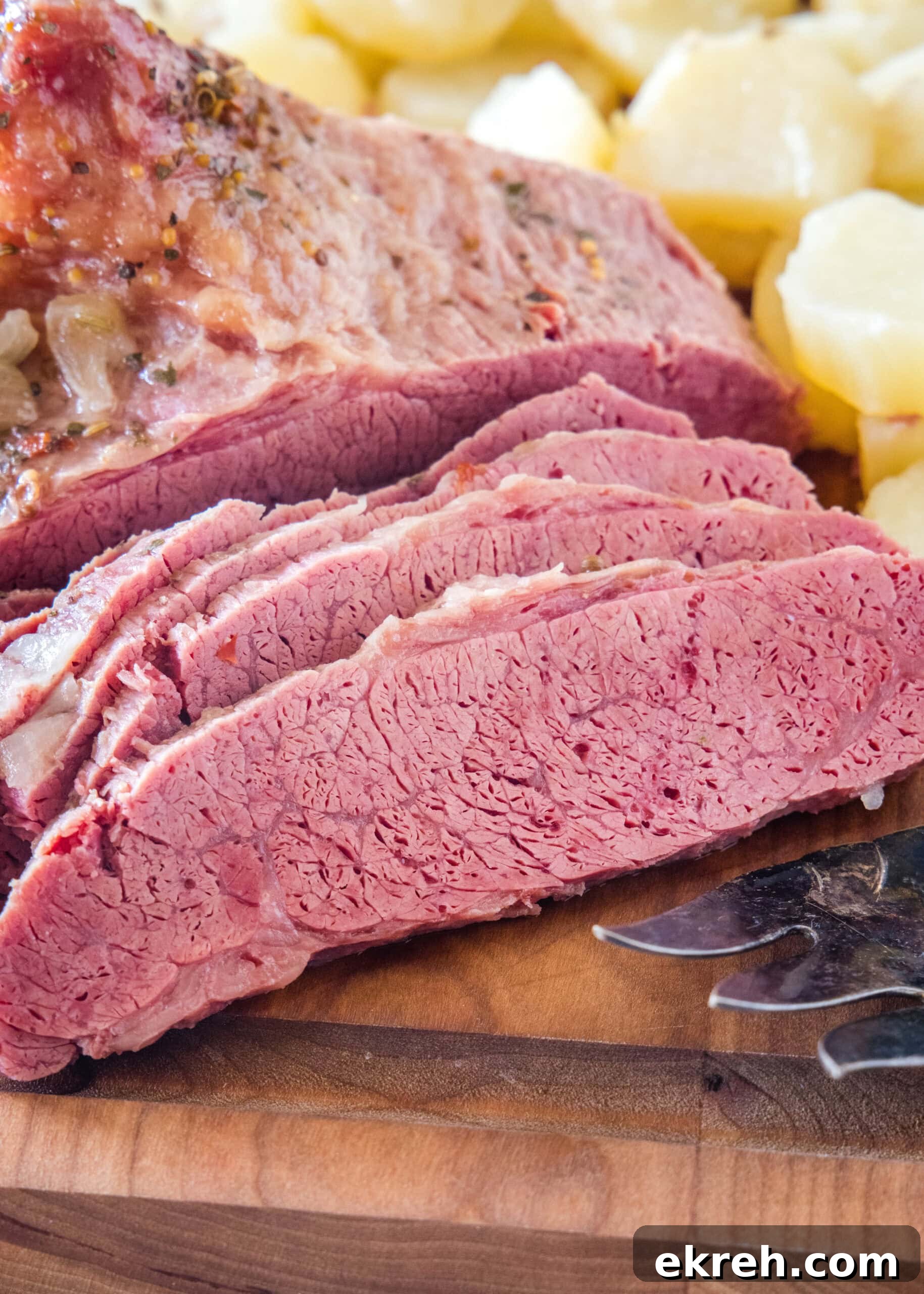 Slow Cooker Corned Beef Sliced corned beef next to cooked onions on a wooden cutting board.