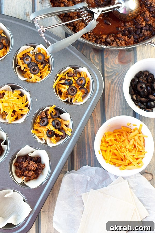 Mini Beef Enchilada Cups Recipe 2 a bowl of beef enchilada mixture along with bowls of cheese and olives beside a cupcake tray housing unbaked enchilada cups ready to be cooked
