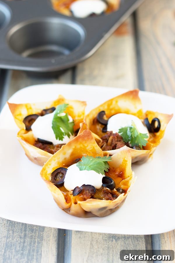 Mini Beef Enchilada Cups Recipe 4 three enchilada cups on a white plate topped with a dollop of sour cream and olives