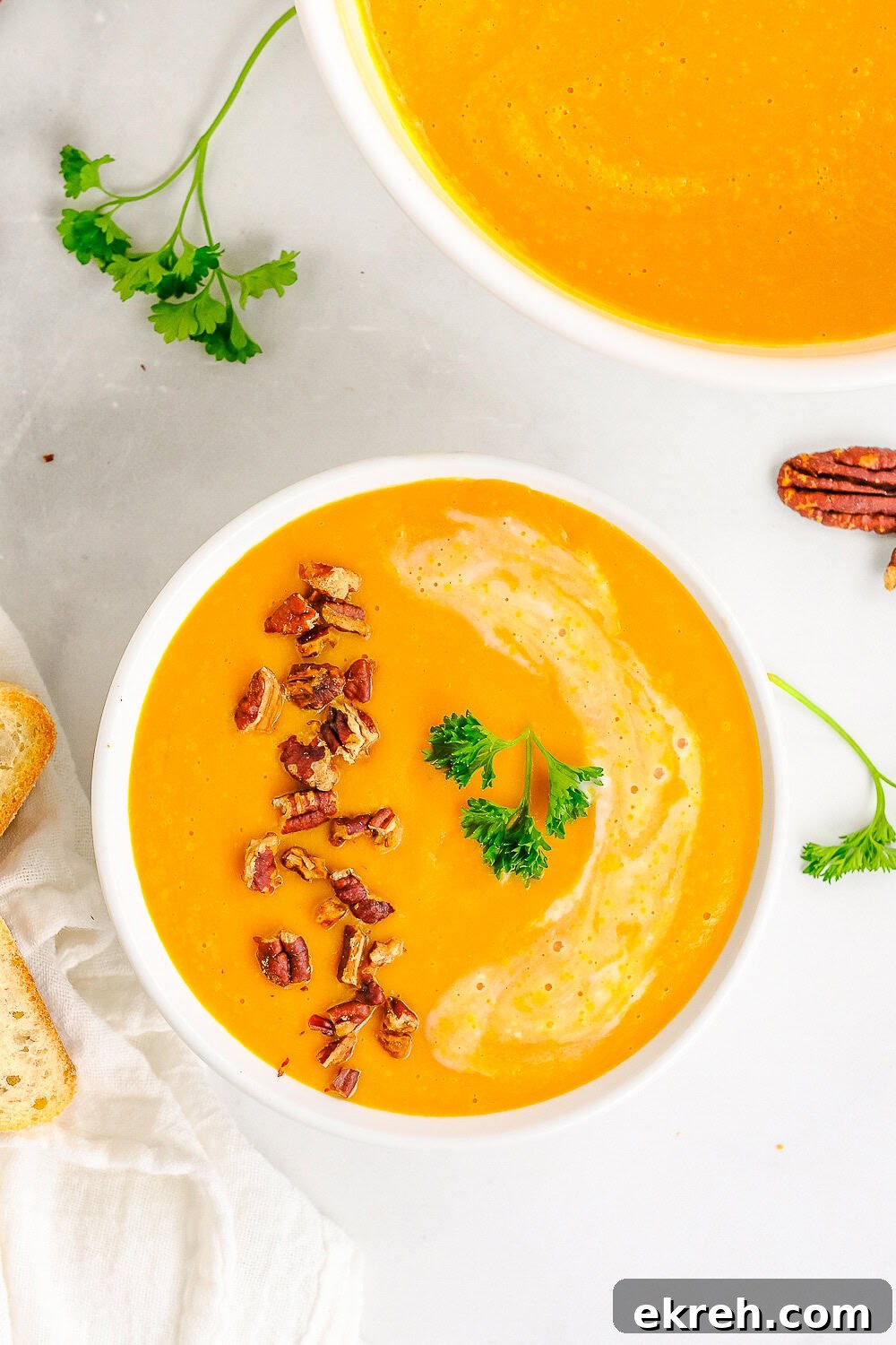 An overhead bowl of creamy carrot soup topped with toasted pecans and parsley.