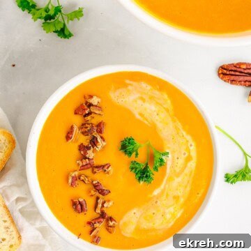 An overhead bowl of creamy carrot soup topped with toasted pecans and parsley.