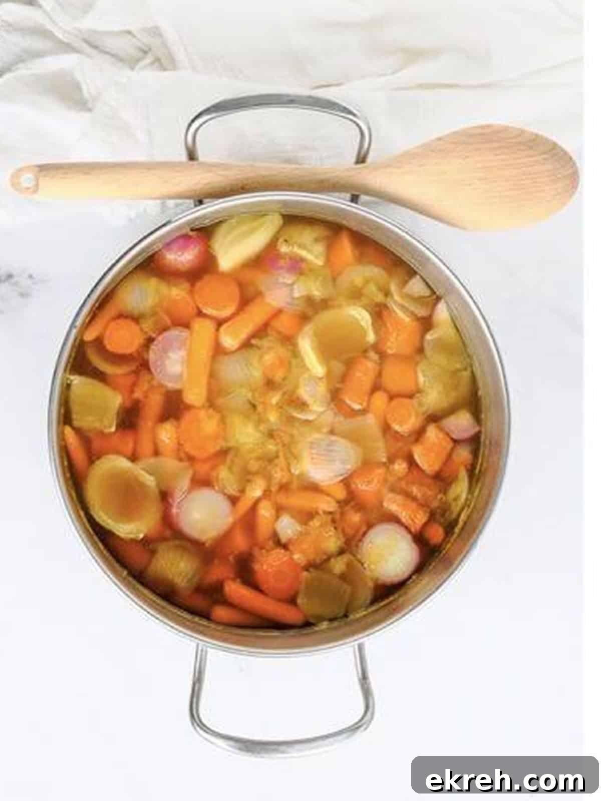 Sliced carrots, onion, radishes, and garlic cooking in vegetable broth in a pot.