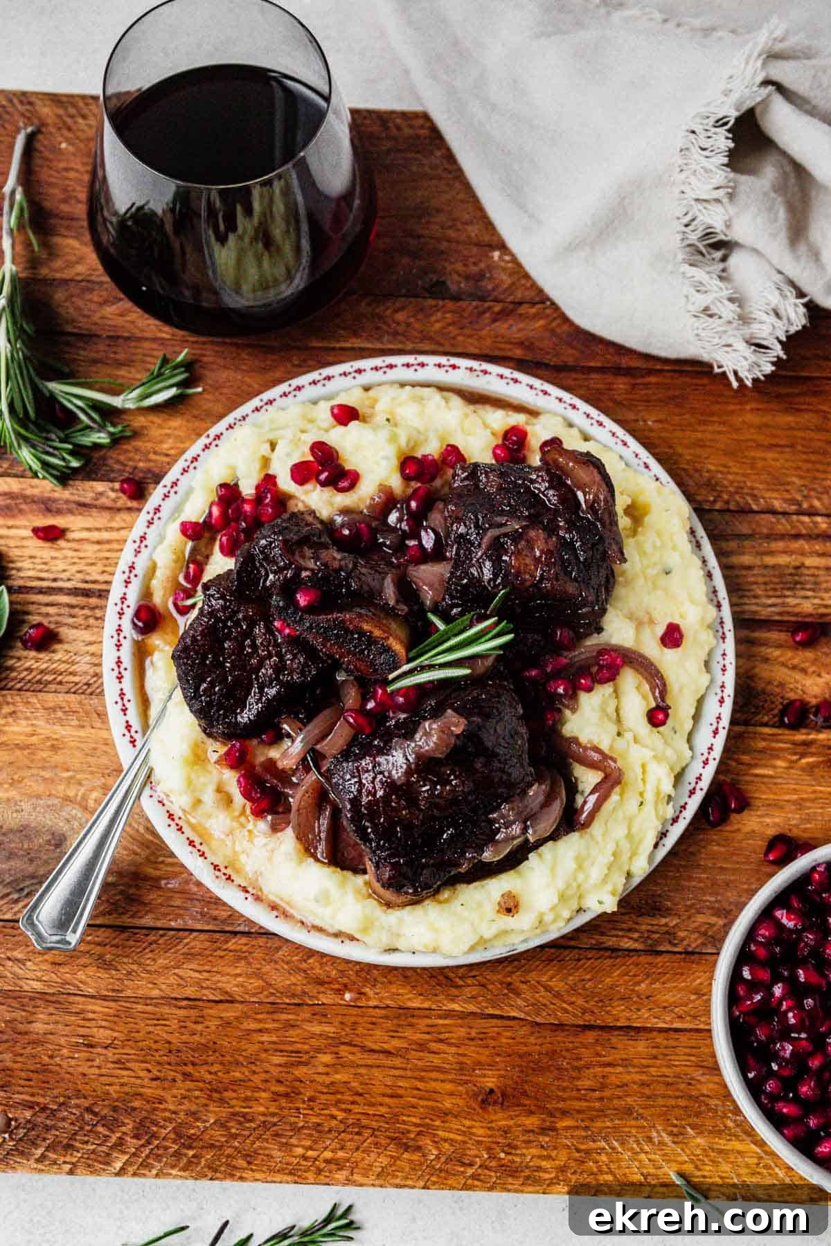 pomegranate short ribs on a plate of mashed potatoes with pomegranate arils on top.