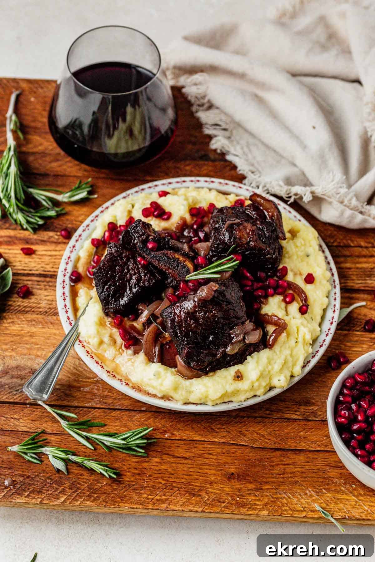 a plate of mashed potatoes and pomegranate short ribs with a glass of red wine.